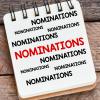 The word 'nominations' on a notepad next to a pencil on a wooden desk